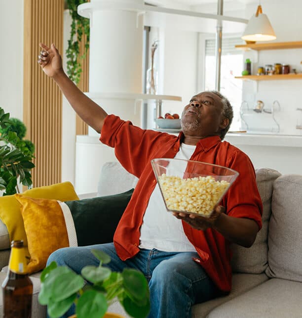 Man sitting on couch with a bowl of popcorn cheering