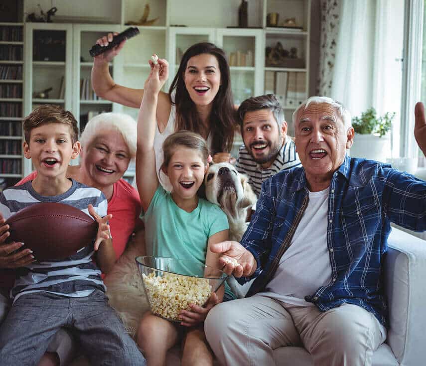Multi-generational family holding a football and popcorn and cheering.