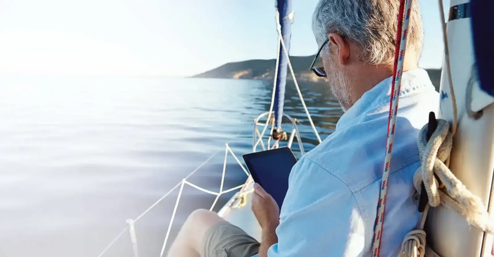 Older man on the bow of a sailboat reading